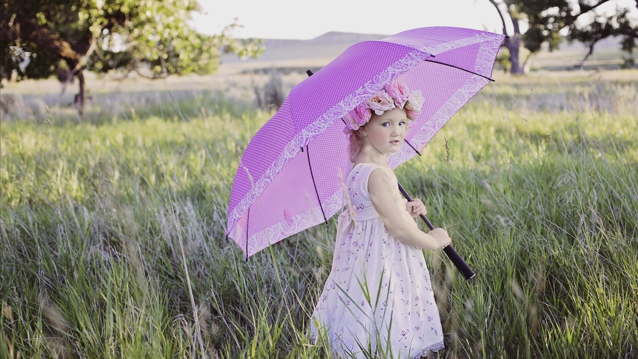 Маленькая девочка стоит в траве с зонтом