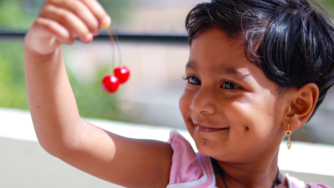 Маленькая улыбающаяся девочка с ягодами вишни в руках