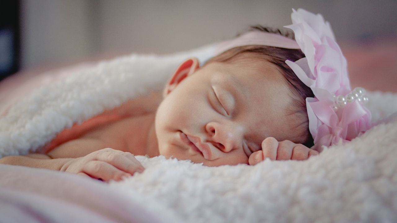 Спящая новорожденная девочка с розовым бантом на голове