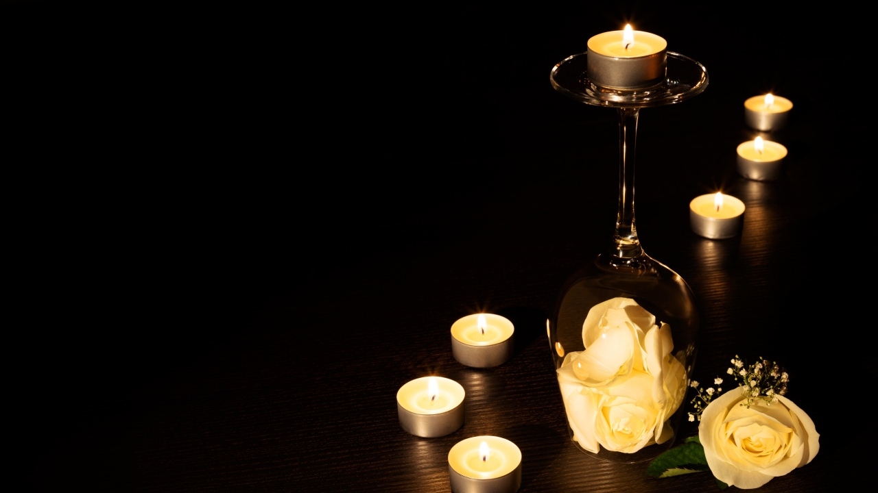 Зажженные свечи с цветами розы на черном фоне