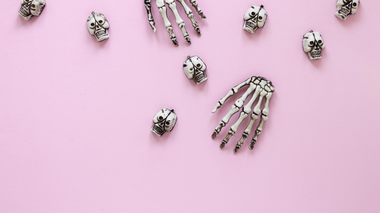 Кисти рук скелета и черепа на розовом фоне