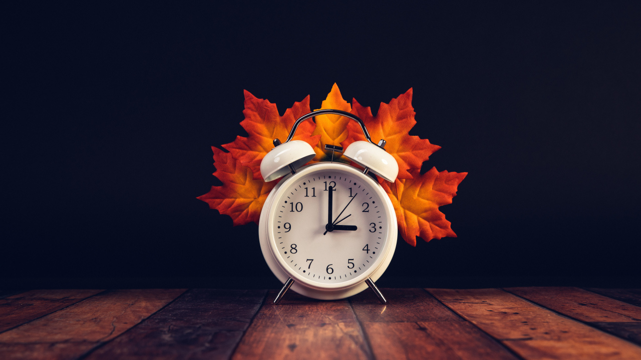 Белый будильник с оранжевыми листьями на столе