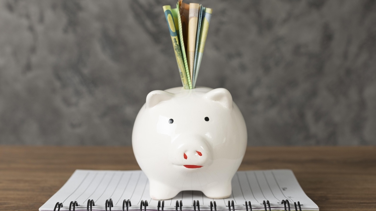 Свинья копилка с купюрами на столе с блокнотом