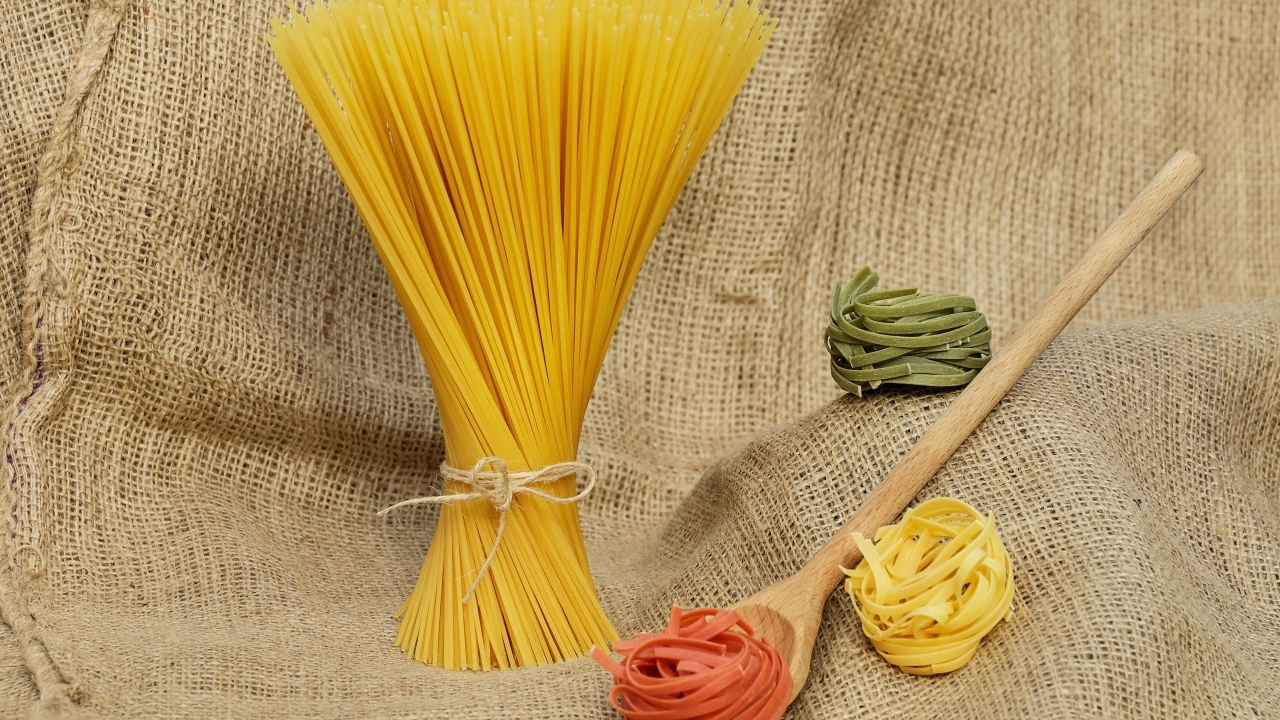 Разноцветные макаронные изделия с деревянной ложкой на мешке