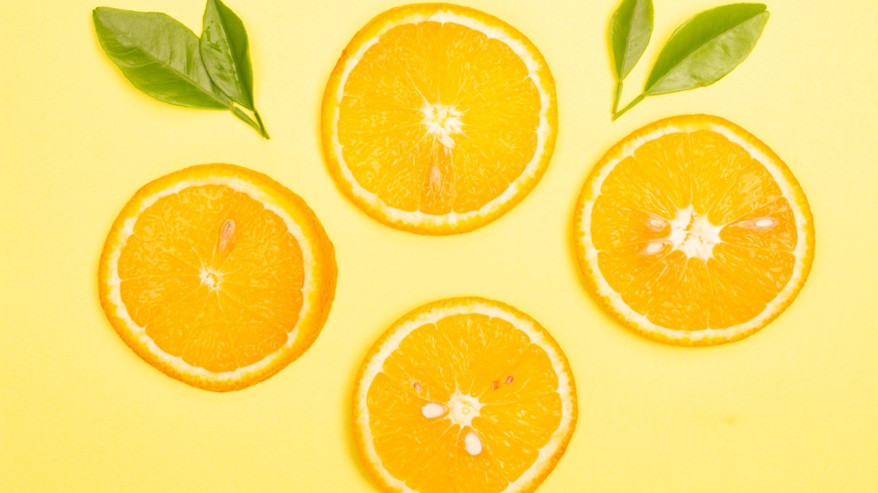 Нарезанный апельсин с зелеными листьями на желтом фоне