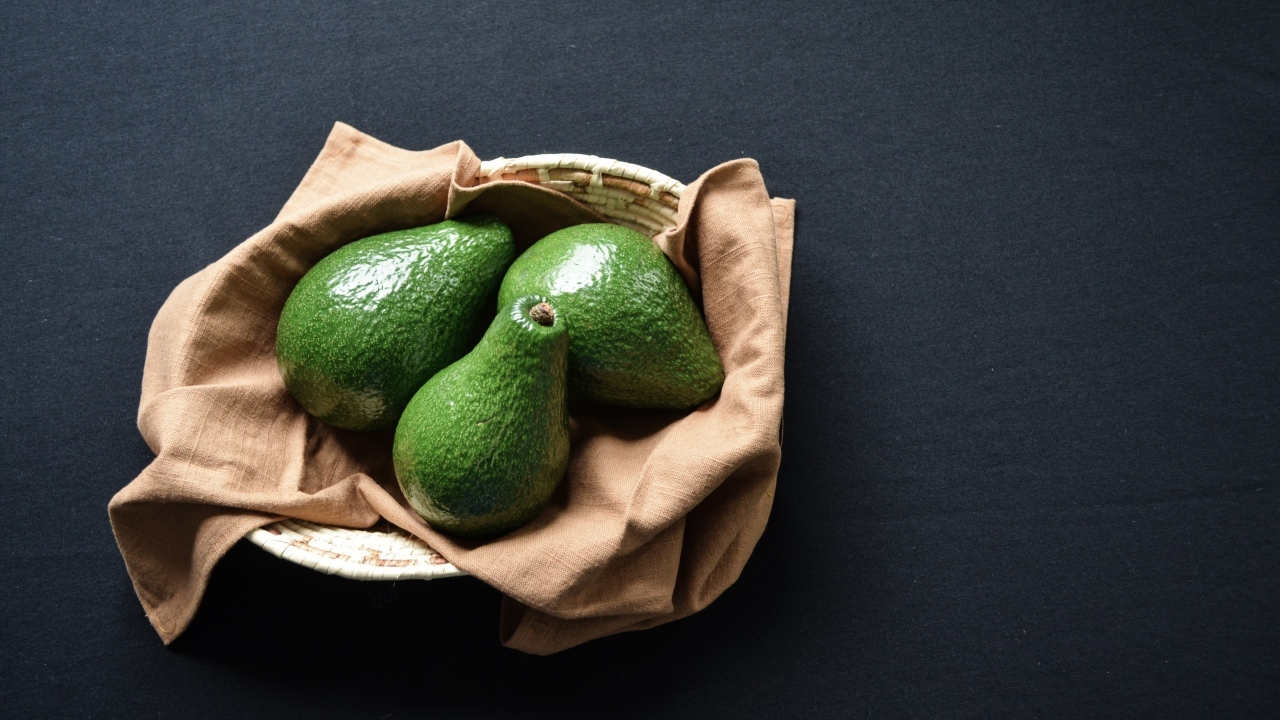 Три зеленых авокадо в корзинке на столе