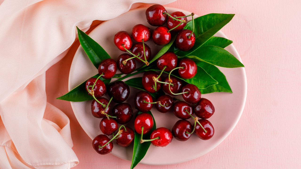 Белая тарелка с красными ягодами черешни на розовом фоне