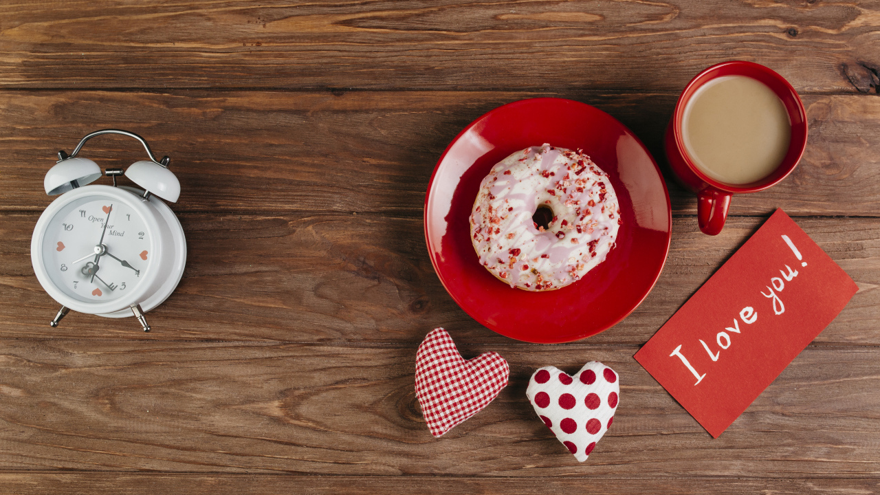 Пончик на столе с будильником, чашкой кофе и сердечками