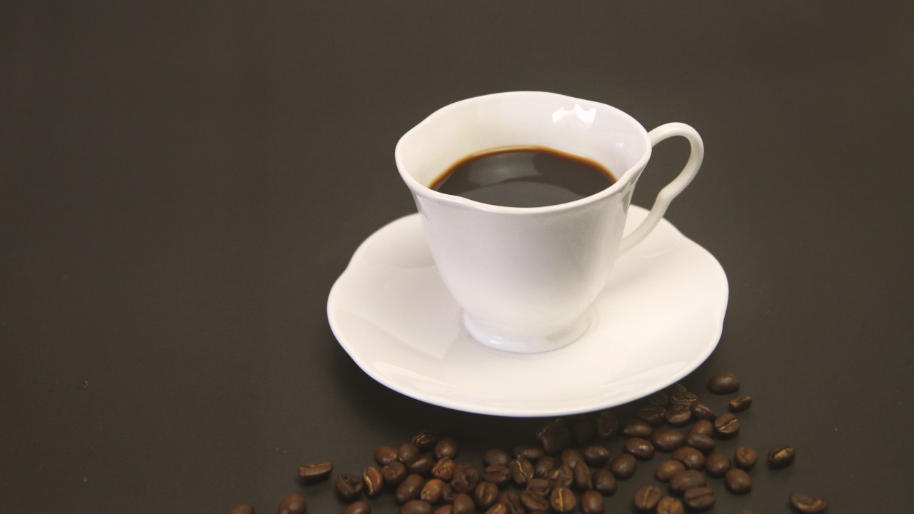 Белая чашка с кофе на столе с зернами