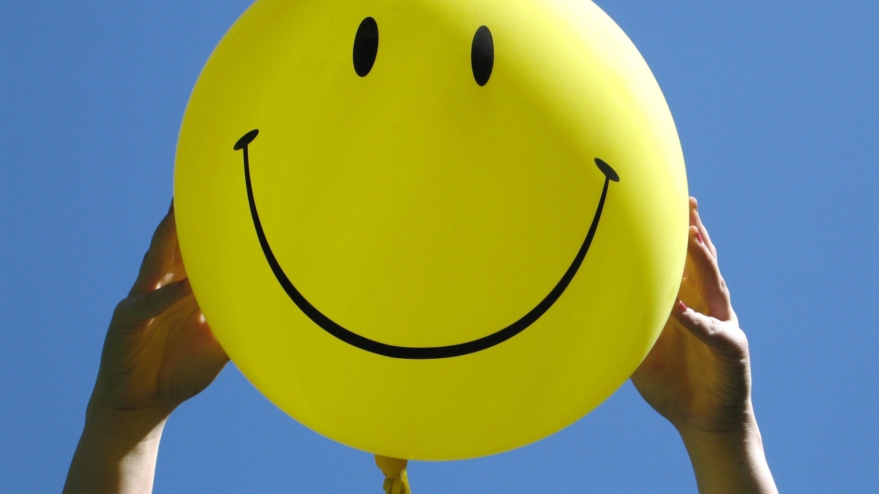 Желтый шарик с улыбкой в руках на голубом фоне