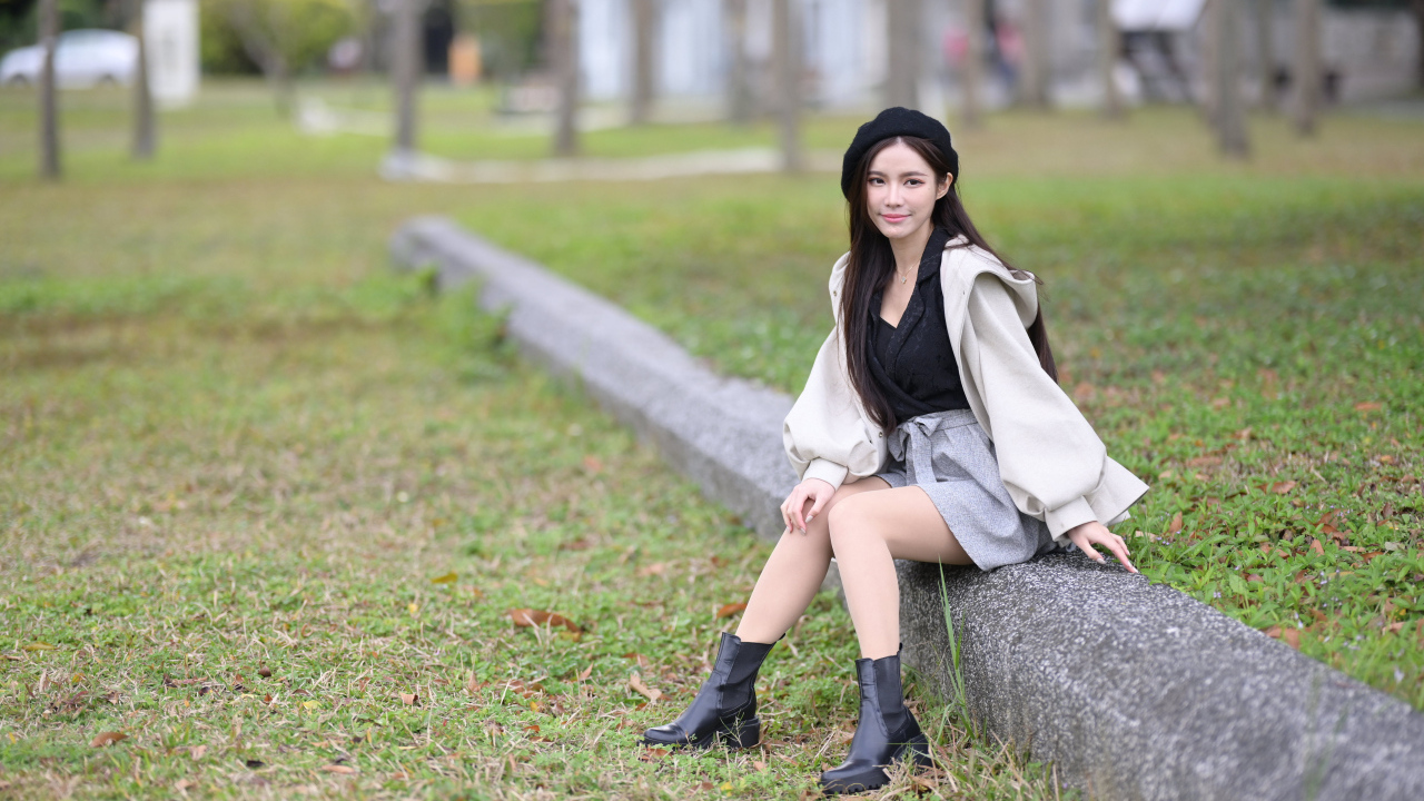 Девушка в пальто сидит на земле в парке