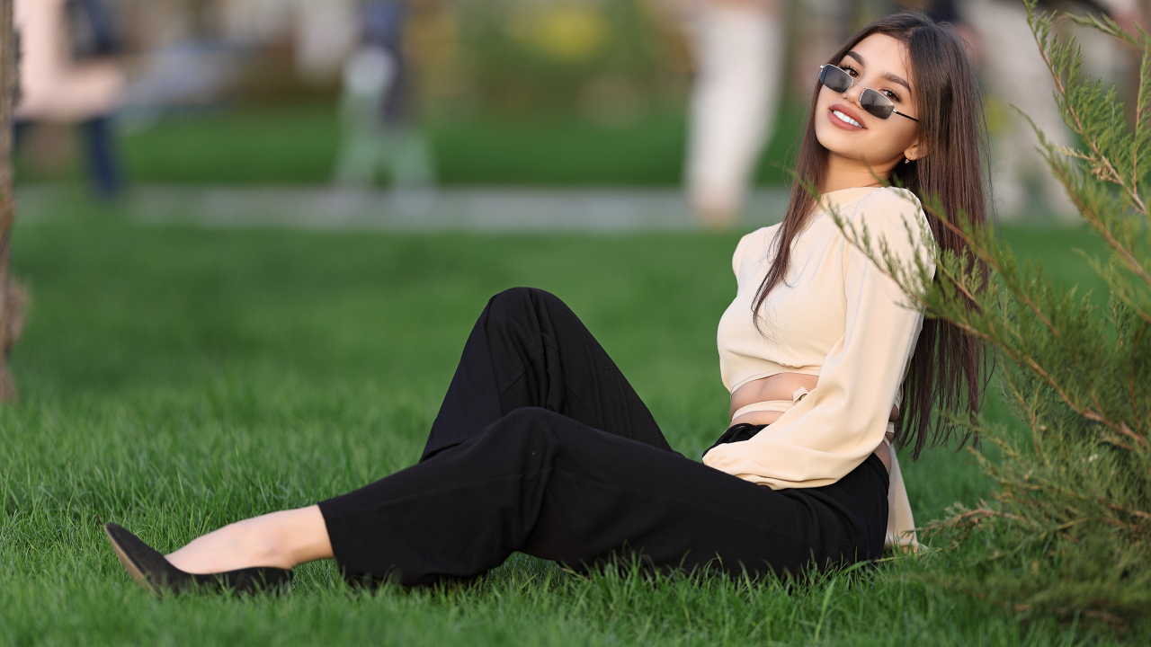 Девушка в черных брюках и блузке сидит на траве