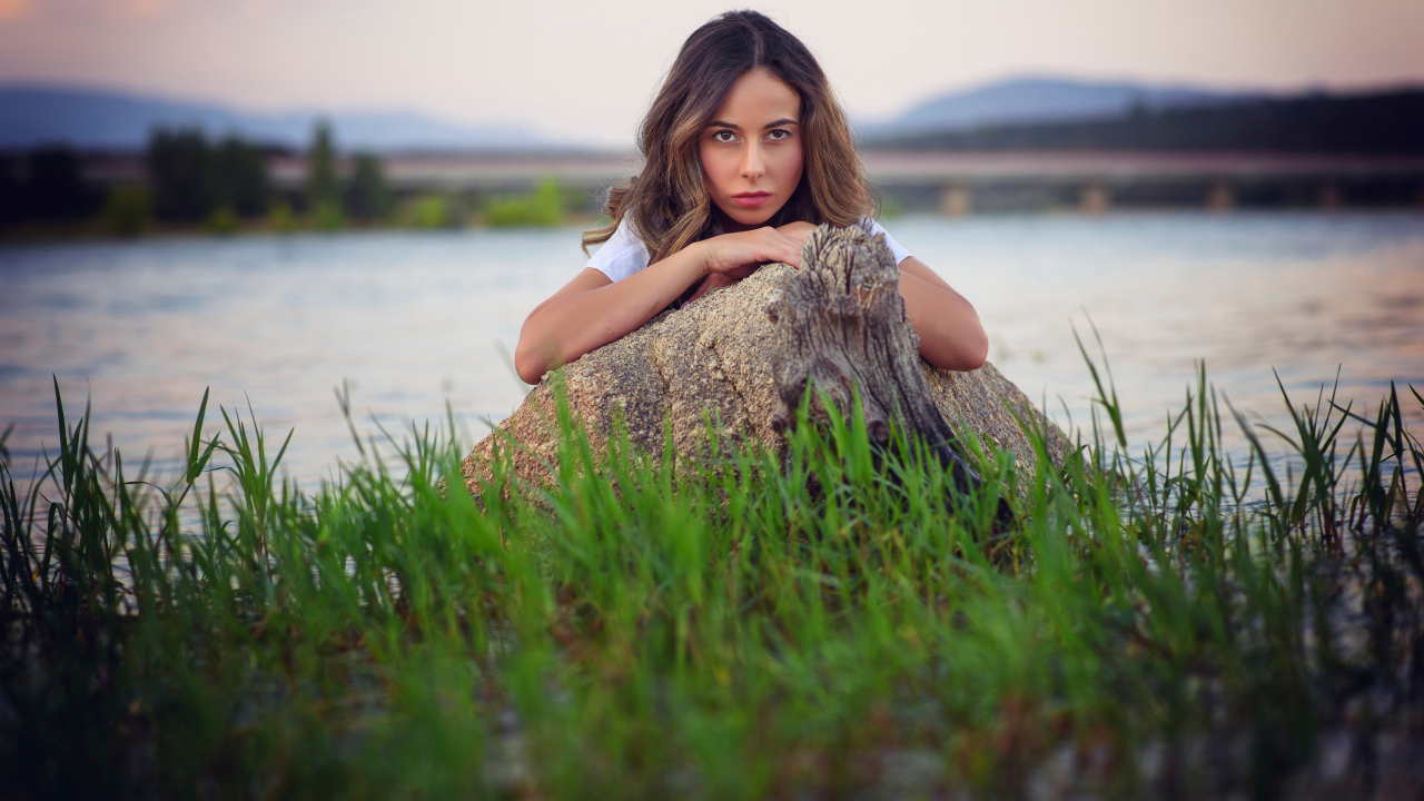 Девушка у воды прячется за камнем