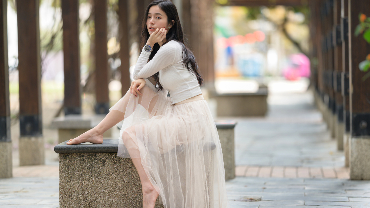 Девушка азиатка в белой юбке из фатина сидит на лавке
