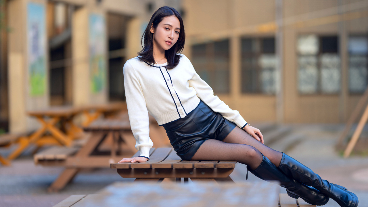 Азиатка сидит на лавке в черных кожаных сапогах