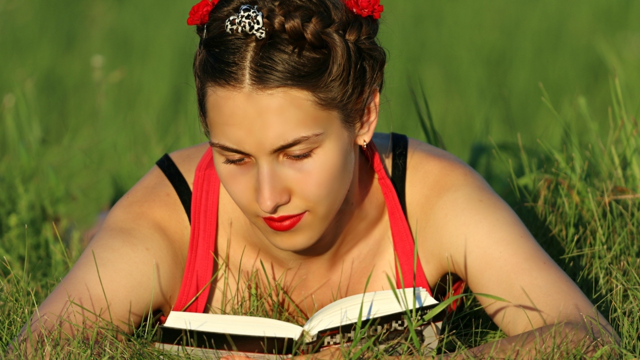 Красивая девушка читает книгу лежа на траве