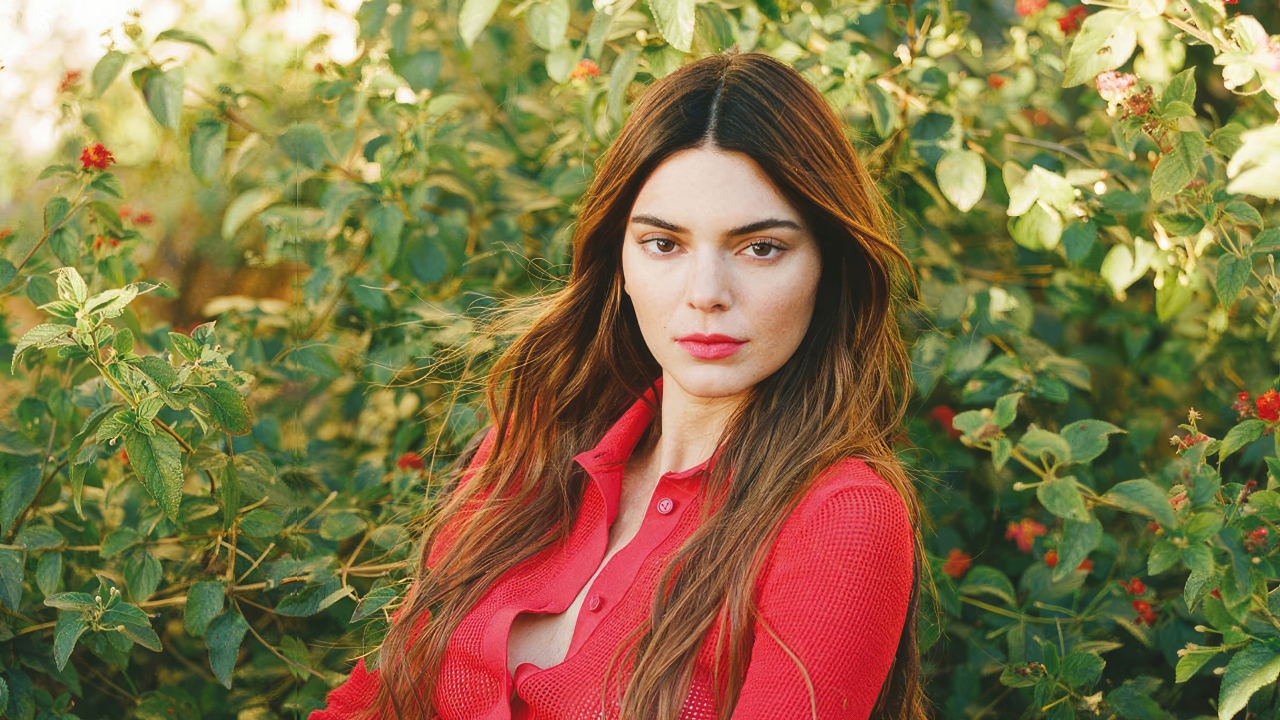 Американская модель Кендалл Дженнер в красной кофте стоит у куста