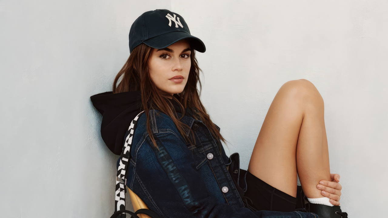 Красивая модель Кайя Гербер в кепке сидит у стены