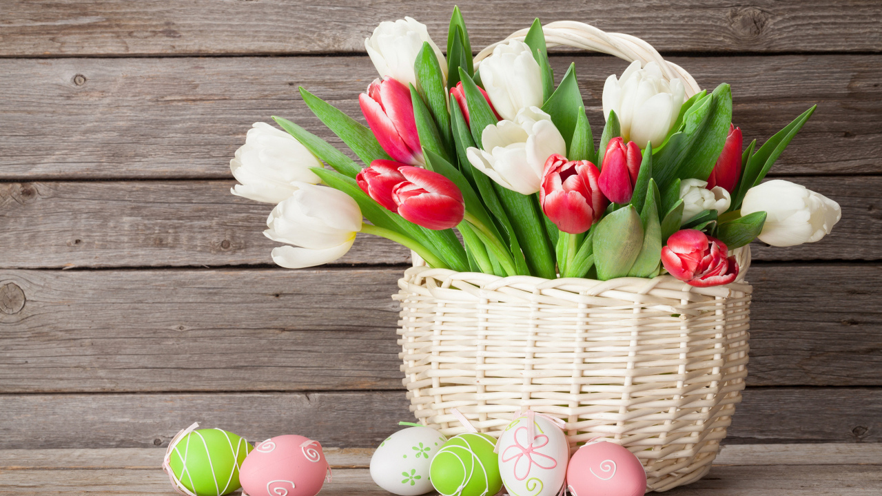 Белые и красные тюльпаны в корзине на столе с разноцветными яйцами на Пасху