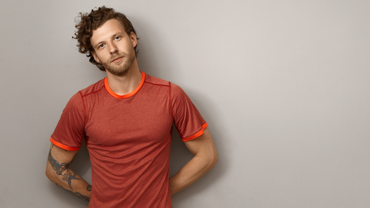 Мужчина в футболке стоит у серой стены