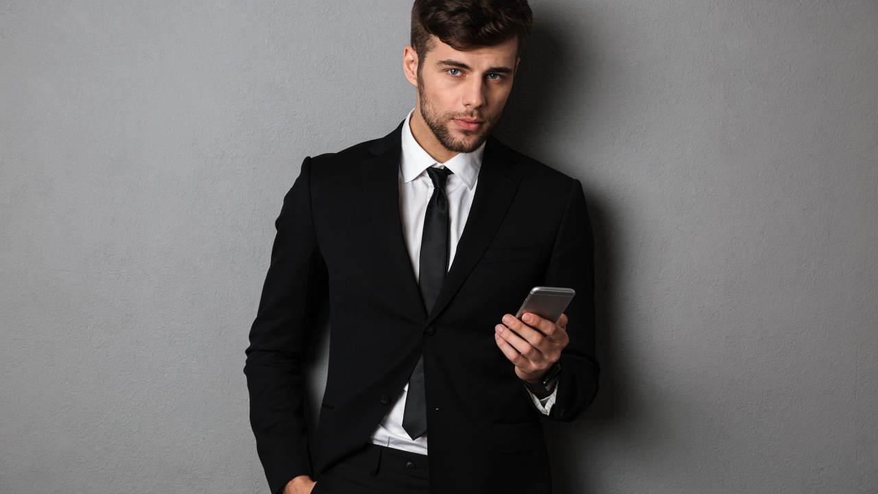 Деловой мужчина в костюме стоит у стены с телефоном