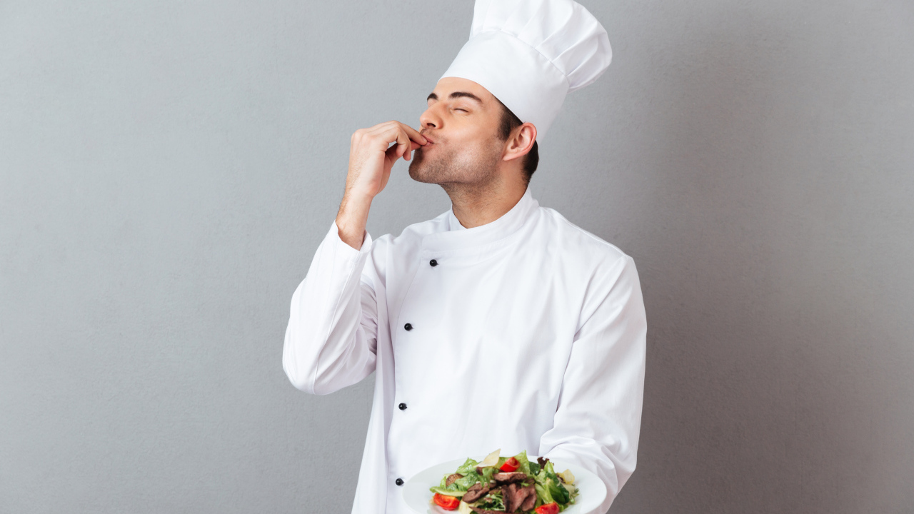 Мужчина повар в белом костюме с блюдом на сером фоне