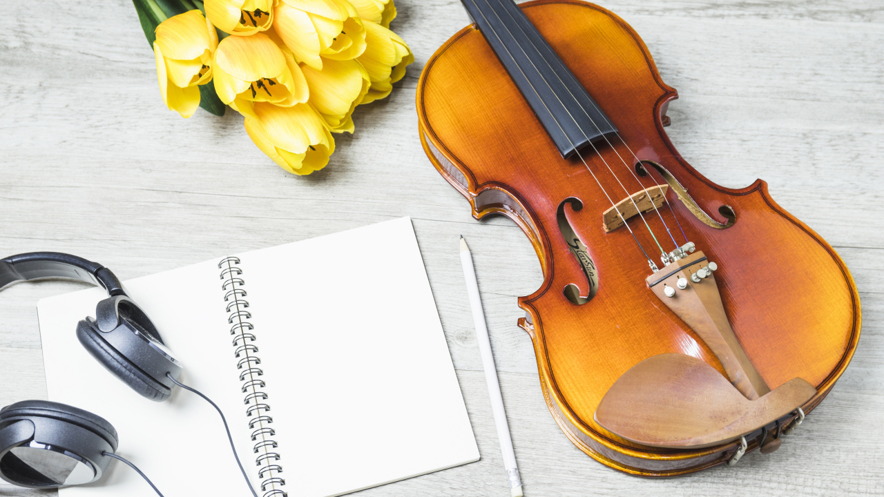 Красивая скрипка на столе с блокнотом, наушниками и букетом тюльпанов