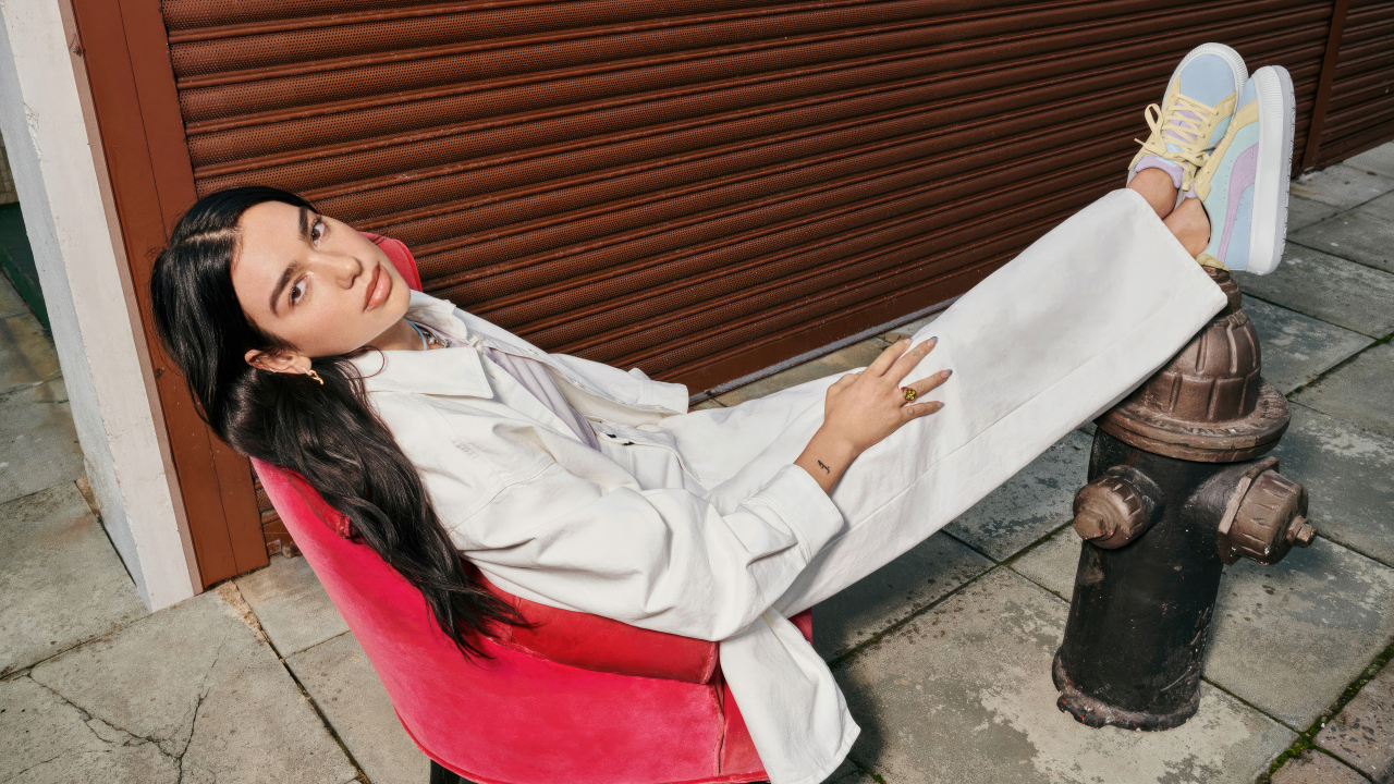 Певица Дуа Липа в белом костюме сидит в кресле