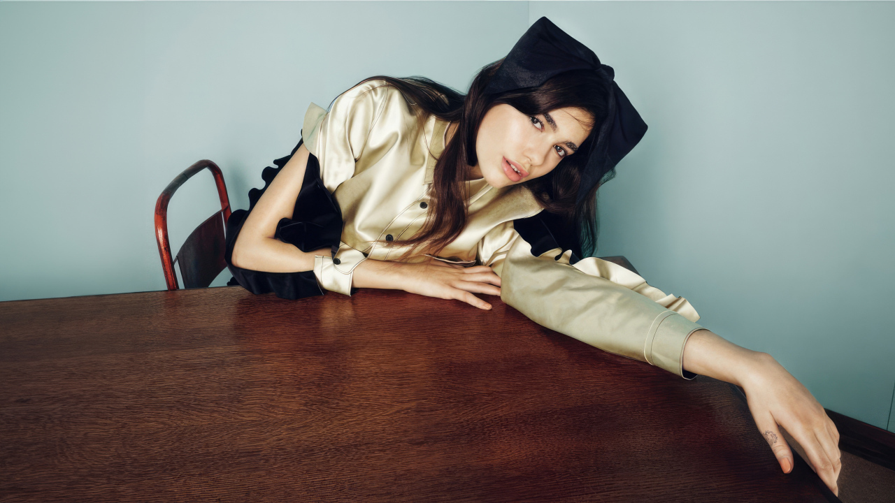 Певица Дуа Липа сидит за деревянным столом