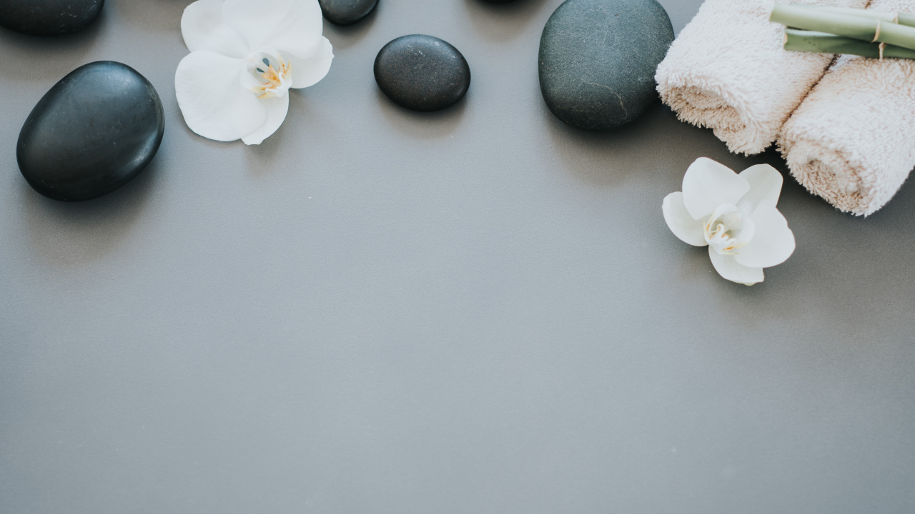 Черные камни с цветами орхидеи и полотенцем на сером фоне