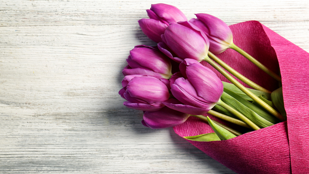 Букет сиреневых тюльпанов в бумаге на столе