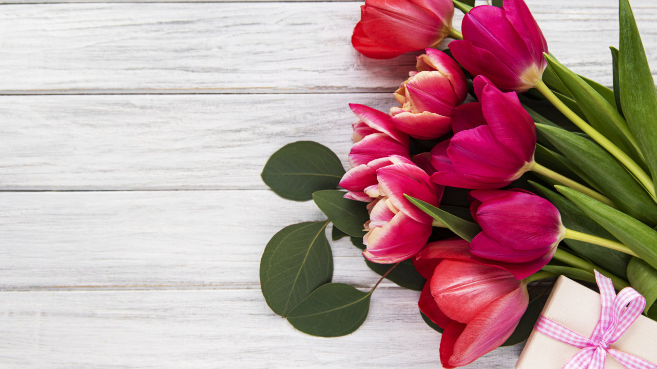 Букет розовых тюльпанов с подарком и зелеными листьями на белом столе