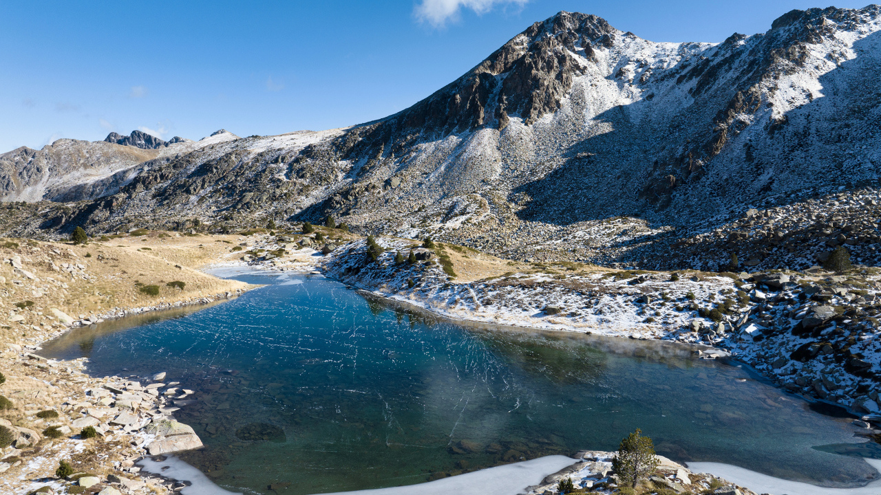 Покрытое льдом озеро в заснеженных горах в лучах солнца, Андорра