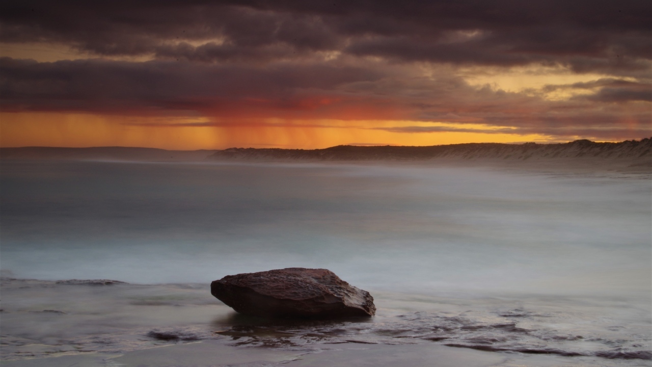 Большой камень в воде на фоне грозового неба в море
