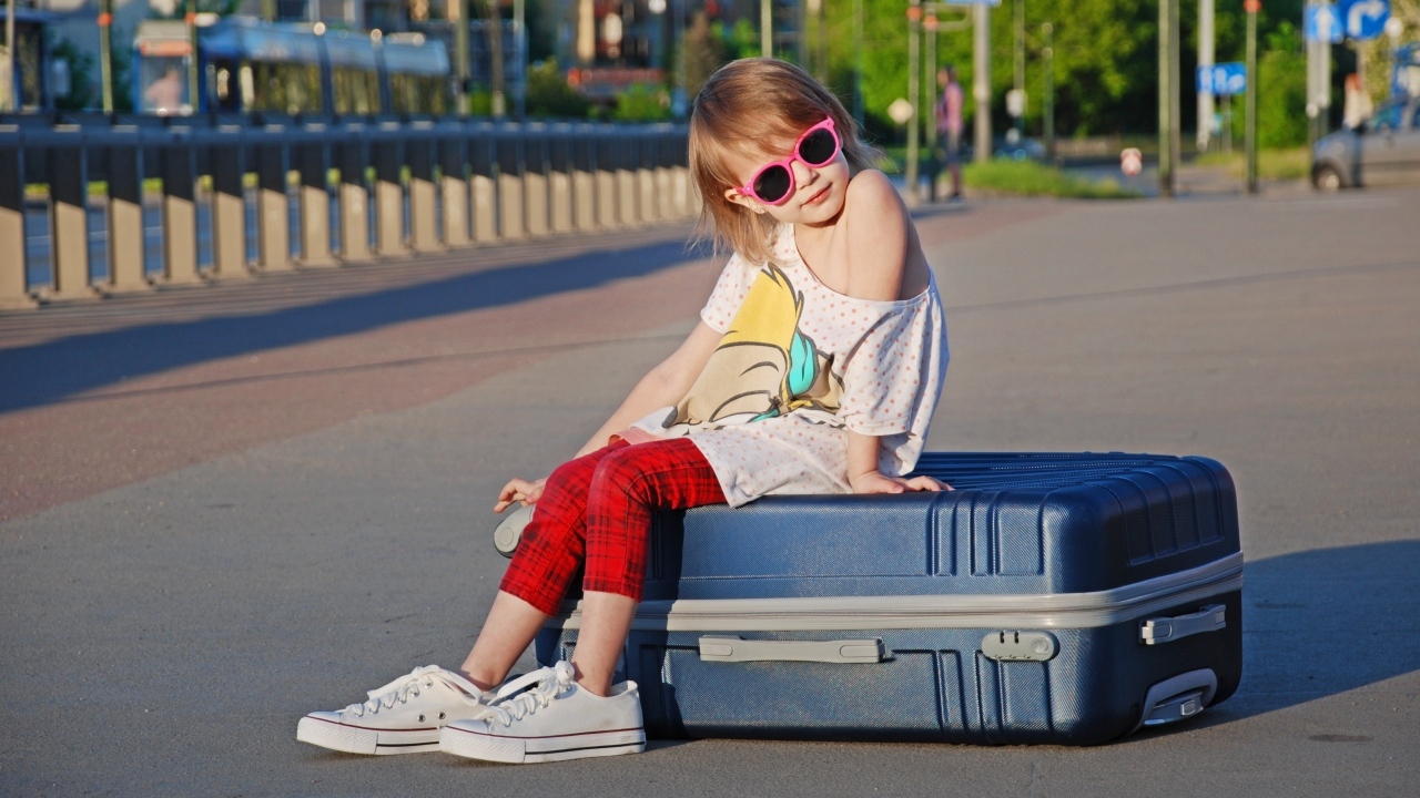 Девочка в солнечных очках сидит на чемодане на дороге