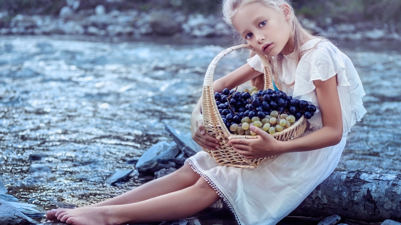 Девочка с корзиной винограда сидит у воды