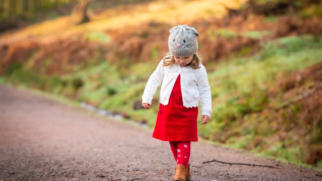Маленькая девочка в красном платье идет по дороге