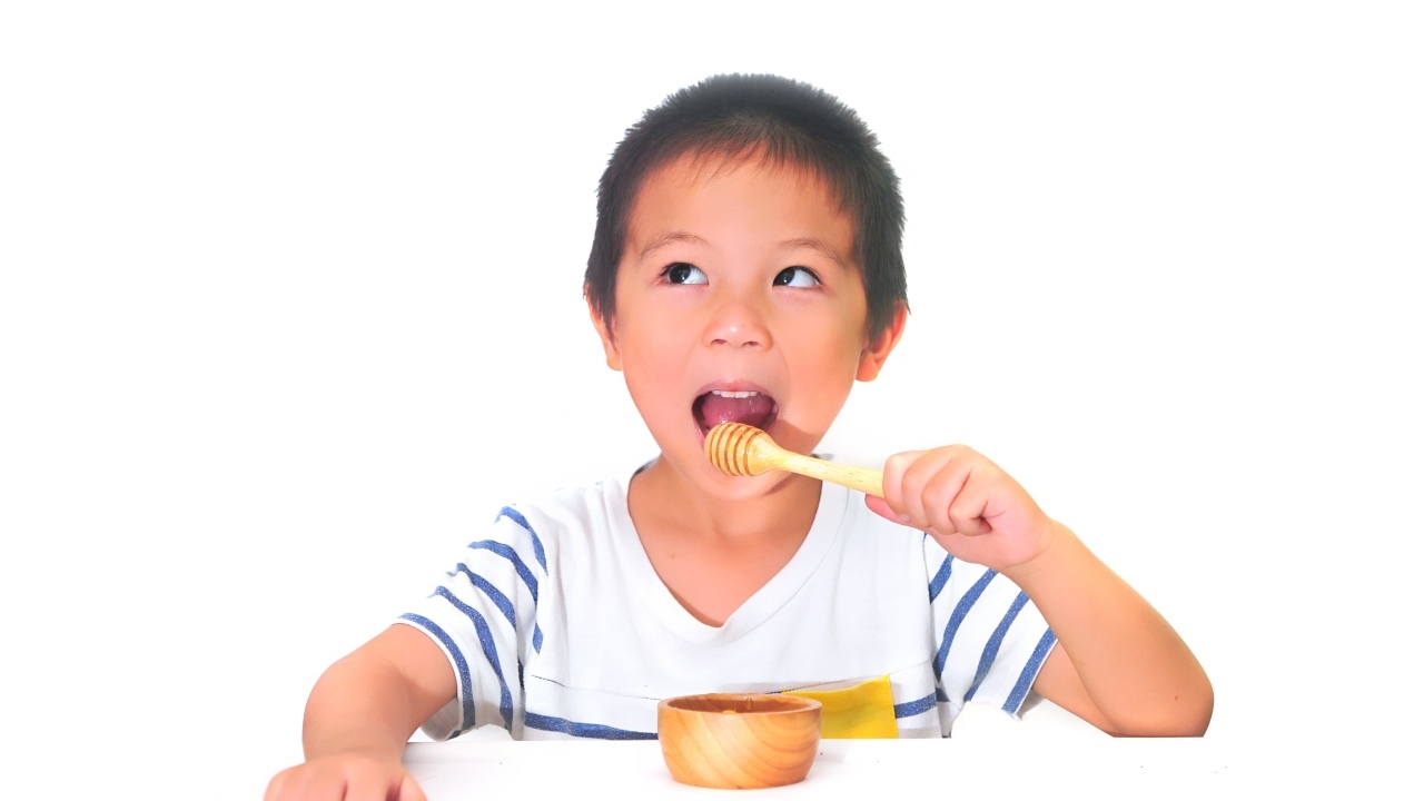 Мальчик азиат ест мед на сером фоне