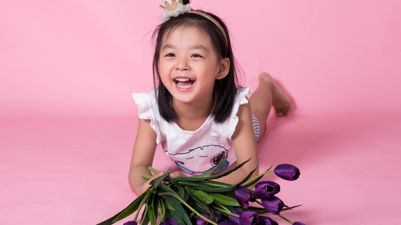 Девочка азиатка в букетом тюльпанов на розовом фоне