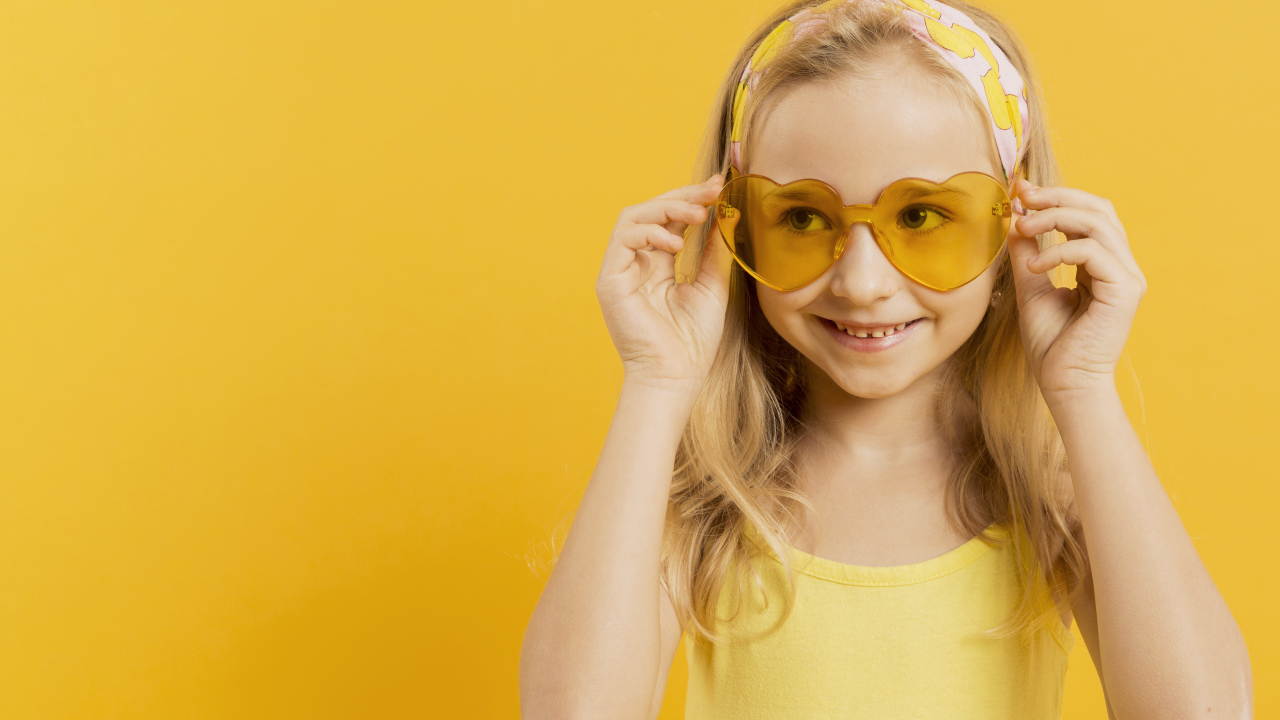 Красивая девочка блондинка в очках в форме сердца на желтом фоне