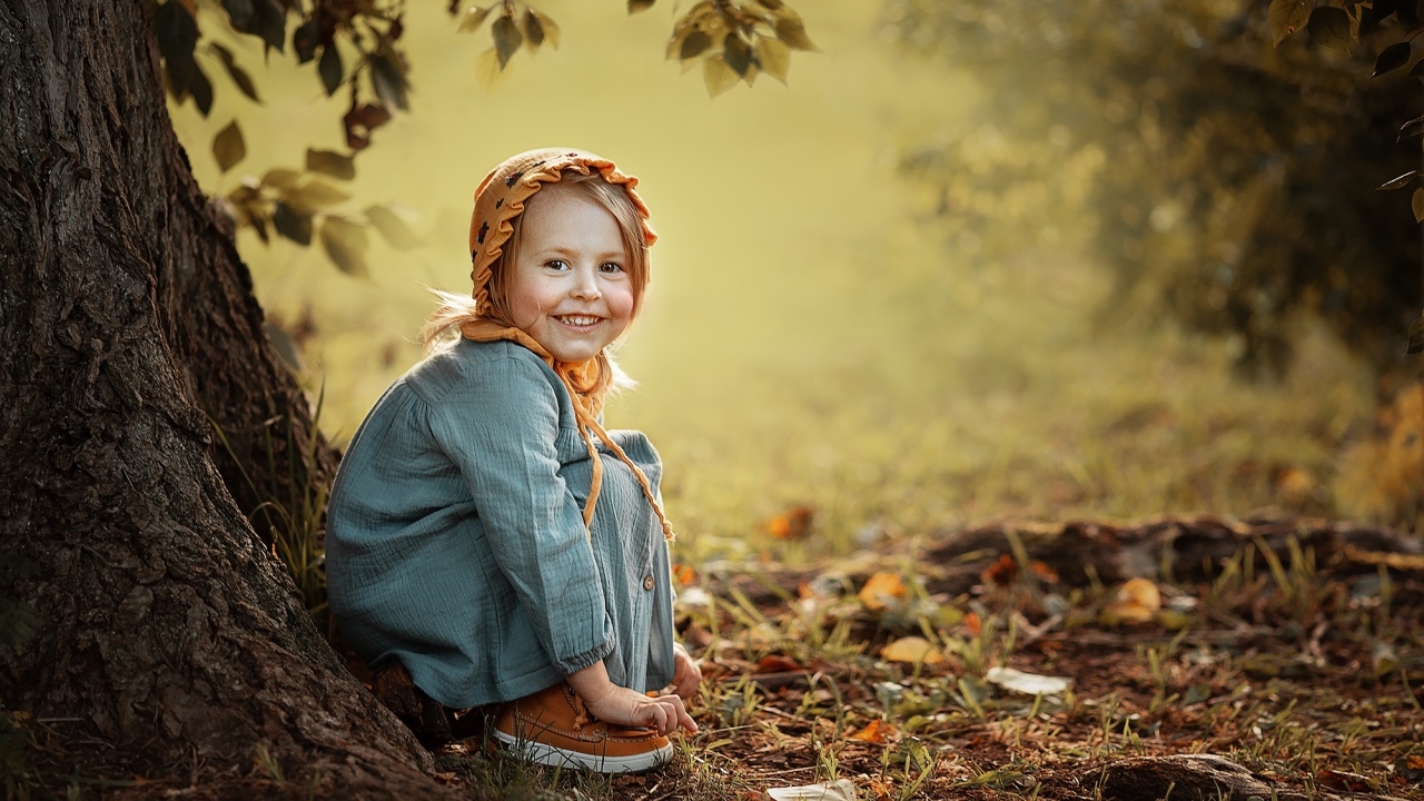 Красивая улыбающаяся девочка сидит под деревом