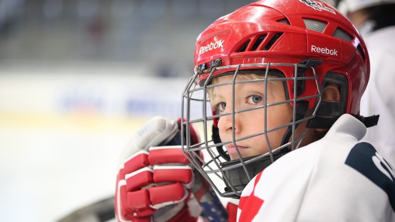Мальчик в красном шлеме хоккеиста на поле