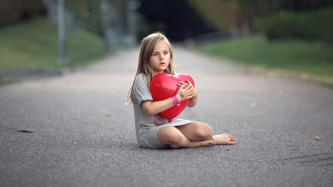 Девочка сидит на дороге с шариком в форме сердца
