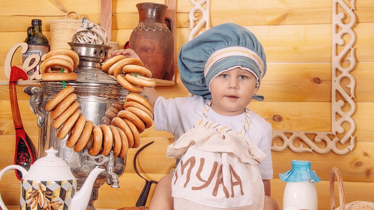 Маленький мальчик повар с продуктами и самоваром на столе