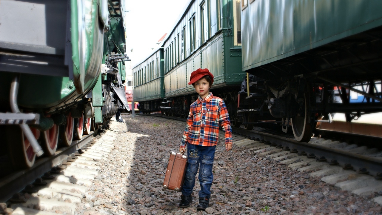 Маленький мальчик с чемоданом у вагонов