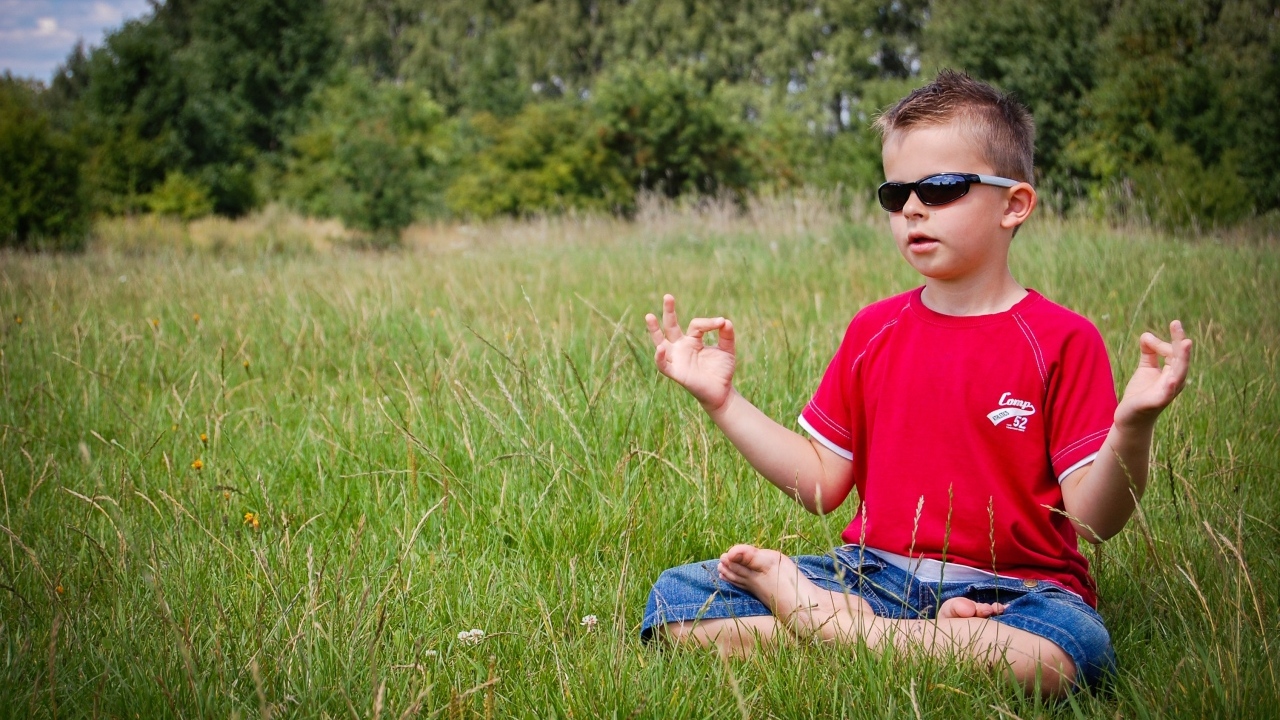 Маленький мальчик в очках медитирует на зеленой траве