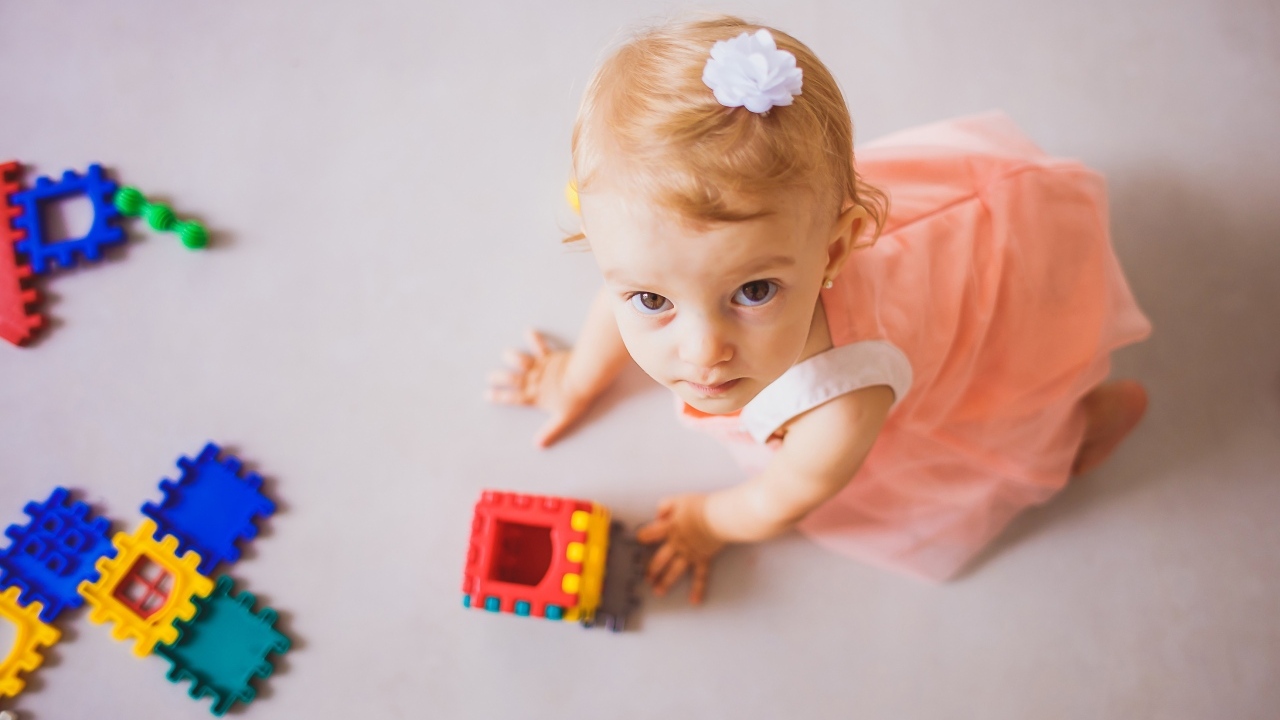 Маленькая девочка играет на полу с конструктором