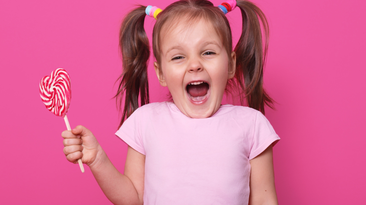 Маленькая девочка с леденцом на розовом фоне