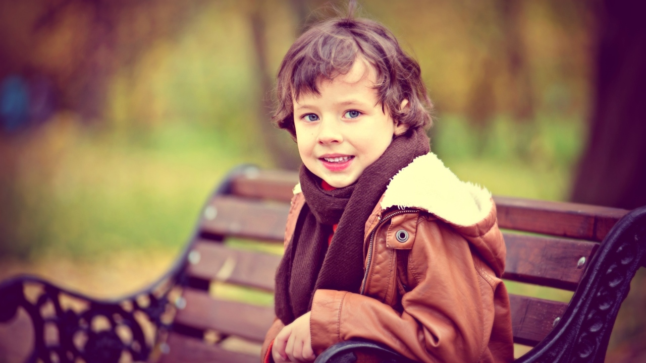 Маленький улыбающийся мальчик на лавке в парке