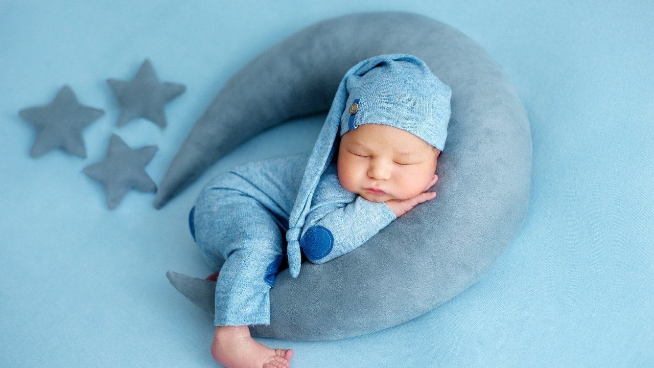 Новорожденный малыш спит на игрушечном полумесяце на голубом фоне